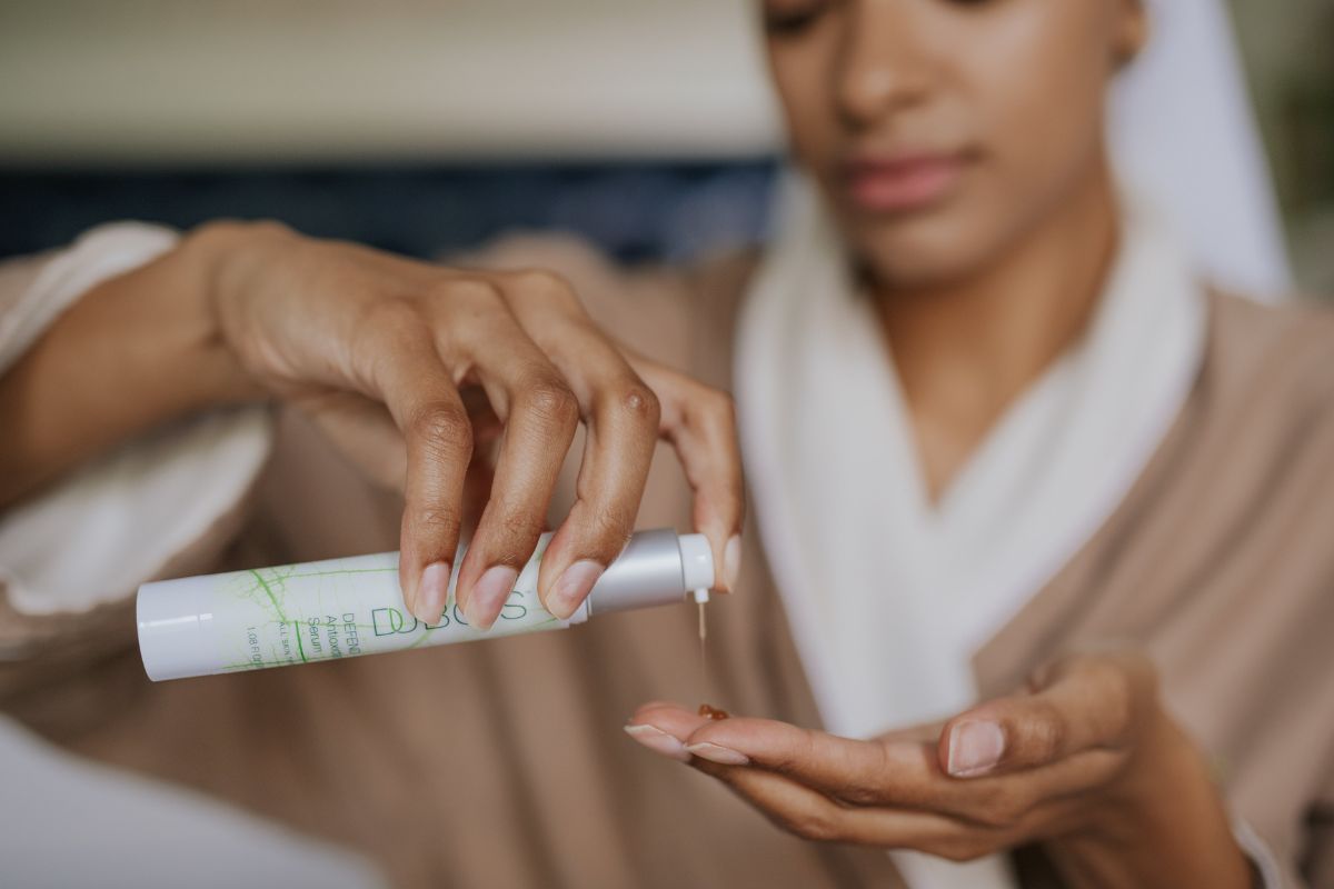 Close-up of graceful hands applying serum from a tube with green graphics, suggesting a calm and relaxing environment.
