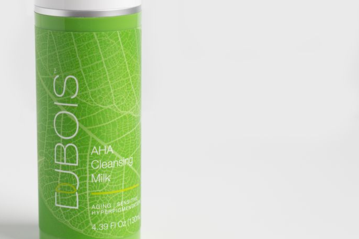 Dubois AHA Cleansing Milk bottle with green leaf design on label. Suitable for aging, sensitive skin, and hyperpigmentation. 4.39 fl oz (130 ml). Background is plain white.