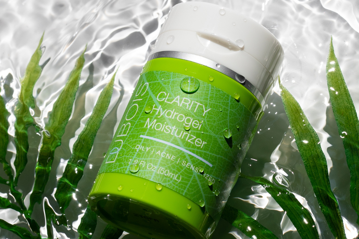 Dubois Clarity Hydrogel Moisturizer bottle in water with green leaves. Designed for oily, acne, and sensitized skin. Fresh, hydrating theme, labeled 1.9 fl oz (50 ml).