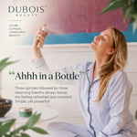 A woman in light blue pajamas spritzes a beauty product from a small bottle, with the brand name DUBOIS BEAUTY and a customer quote overlaid on the image.
