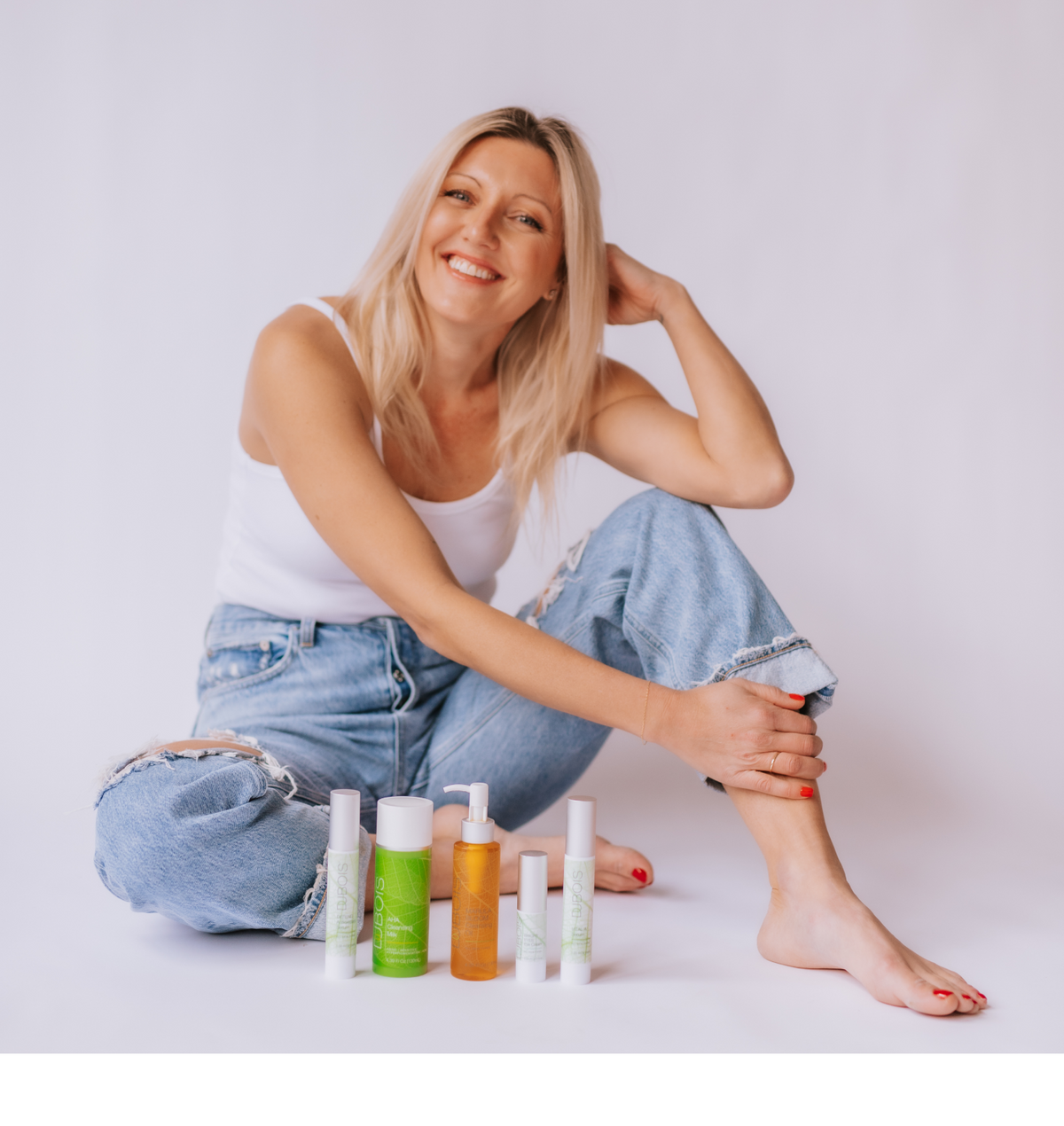 woman wearing jeans smiling with dubois beauty products in front of her